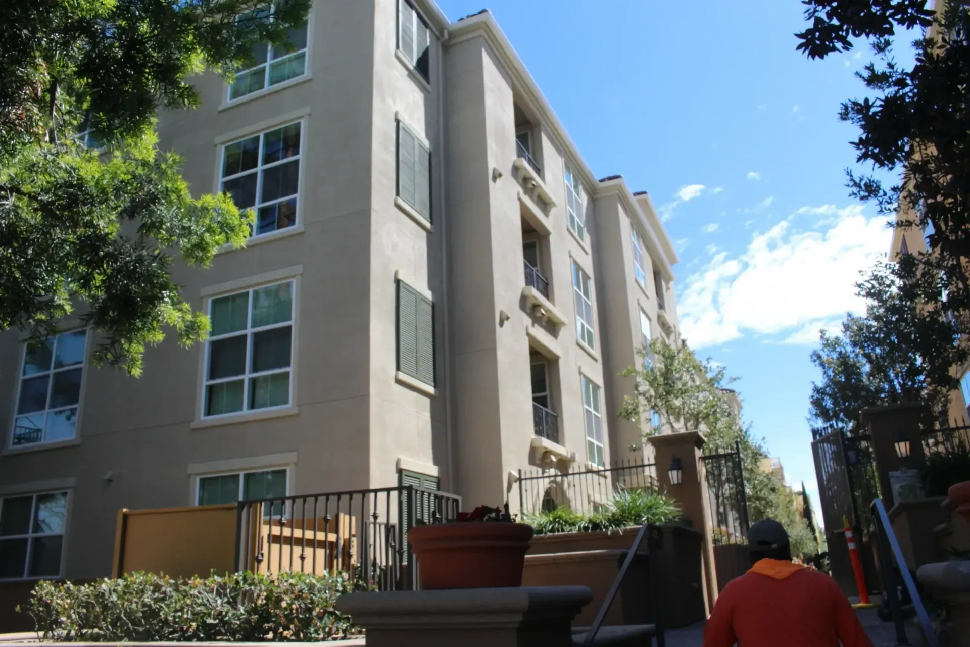 Apartment buildings along a sunny walkway with trees and a person in an orange shirt