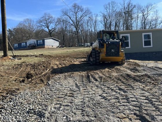A yellow tractor with a black bucket is moving dirt on a road.