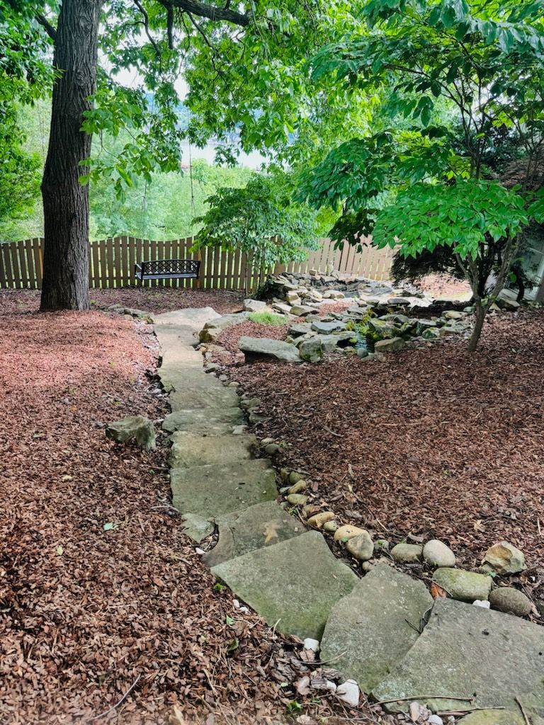 A stone path leading to a wooden fence surrounded by trees and rocks.