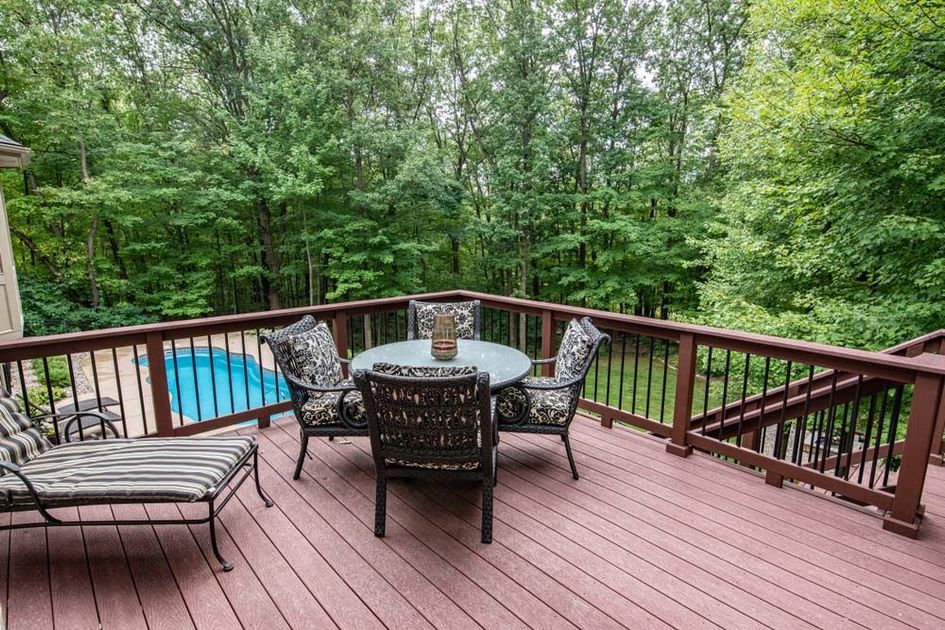 A deck with a table and chairs and a pool in the background.