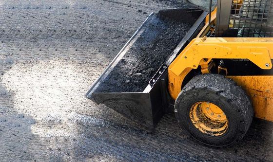 A yellow tractor with a black bucket is moving dirt on a road.