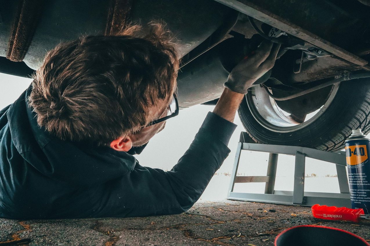 Mechanic working under a car, wearing glasses and gloves.