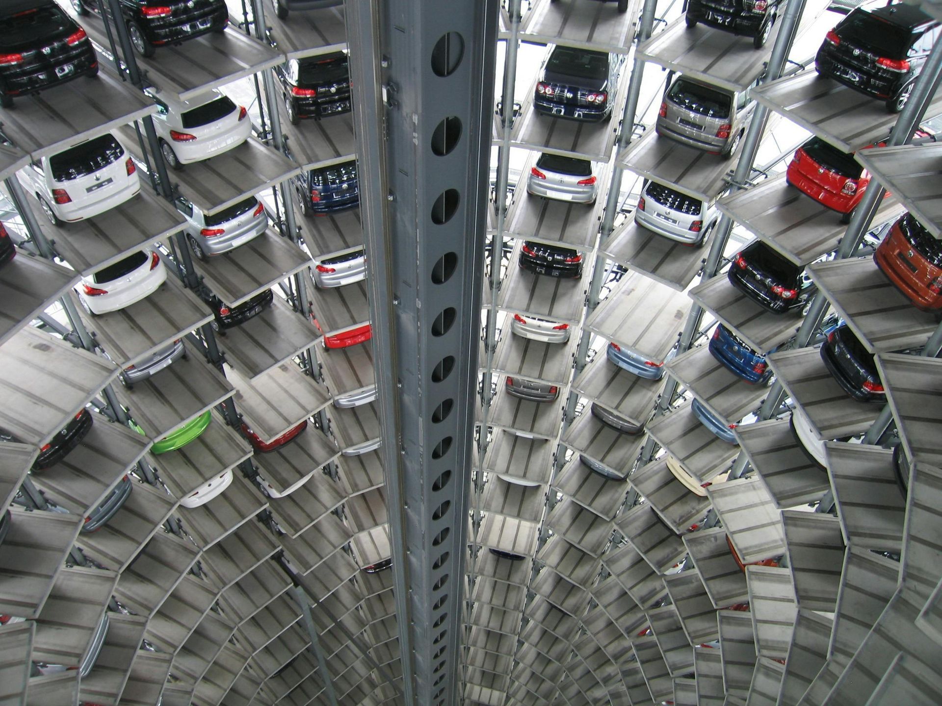 Vertical car parking tower with many vehicles parked on circular levels. Central metal support.