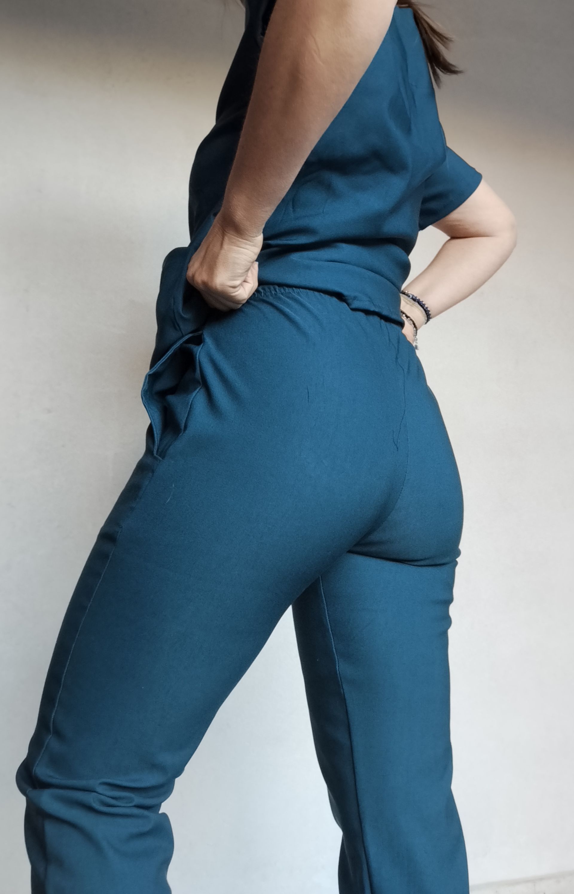 Persona con uniforme verde azulado apoyada contra una pared blanca.