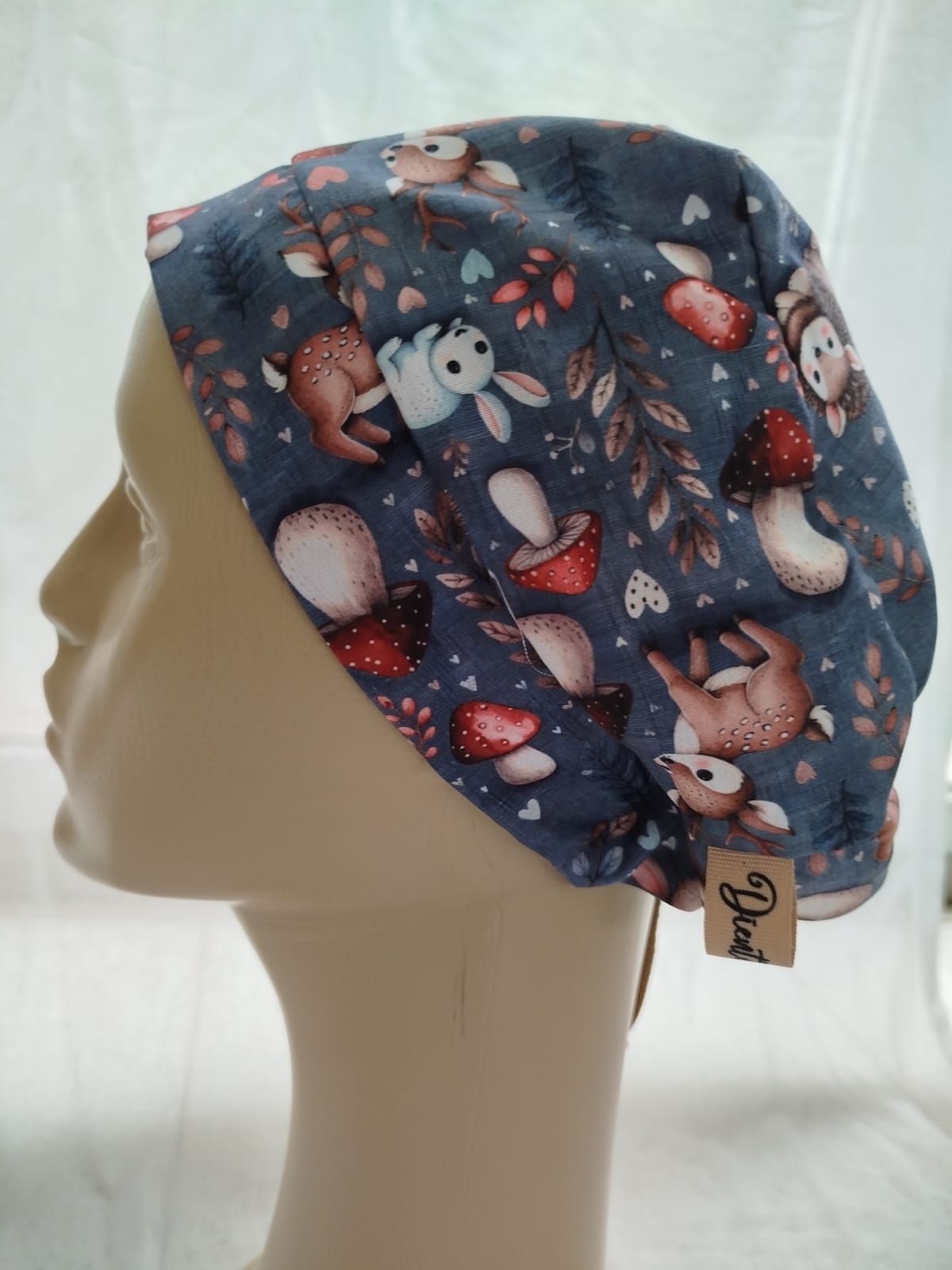 Una gorra con estampado de animales del bosque, incluidos ciervos y conejos, sobre una cabeza de maniquí.