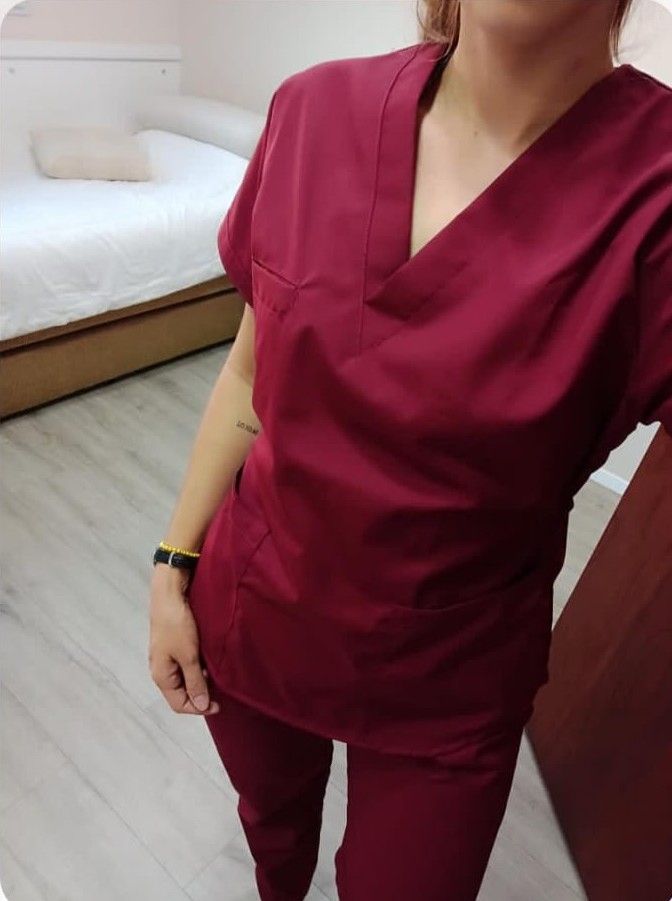 Una persona con uniforme médico color granate se encuentra en un interior. El entorno incluye una cama y un armario.