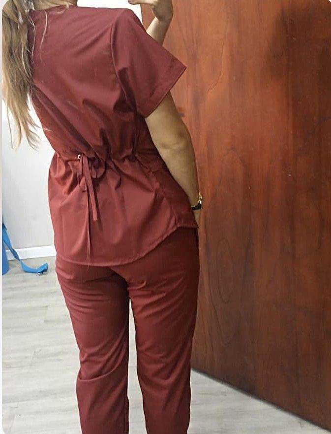 Una persona con uniforme médico color granate se encuentra en un interior. El entorno incluye una cama y un armario.