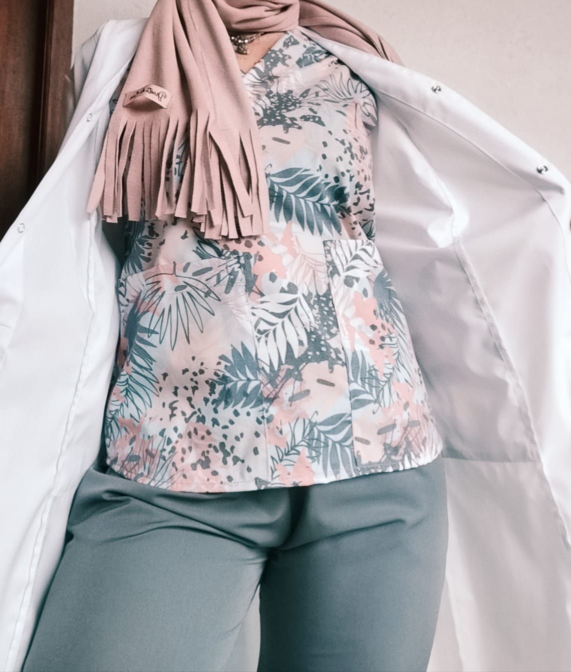 Mujer con top con estampado tropical, pantalón gris y abrigo blanco, luciendo una bufanda rosa.