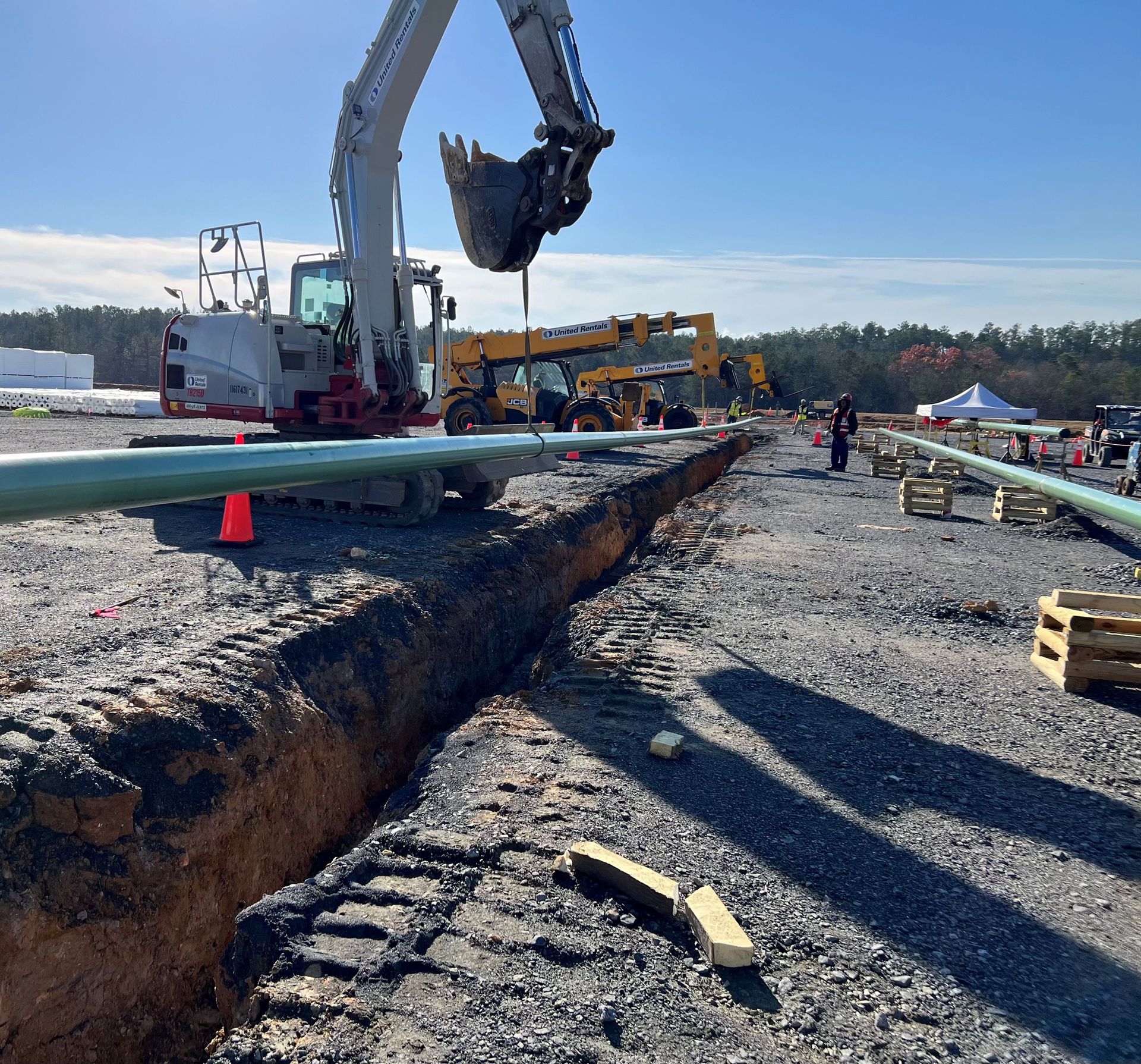 Two men are standing in the dirt holding metal pipes.