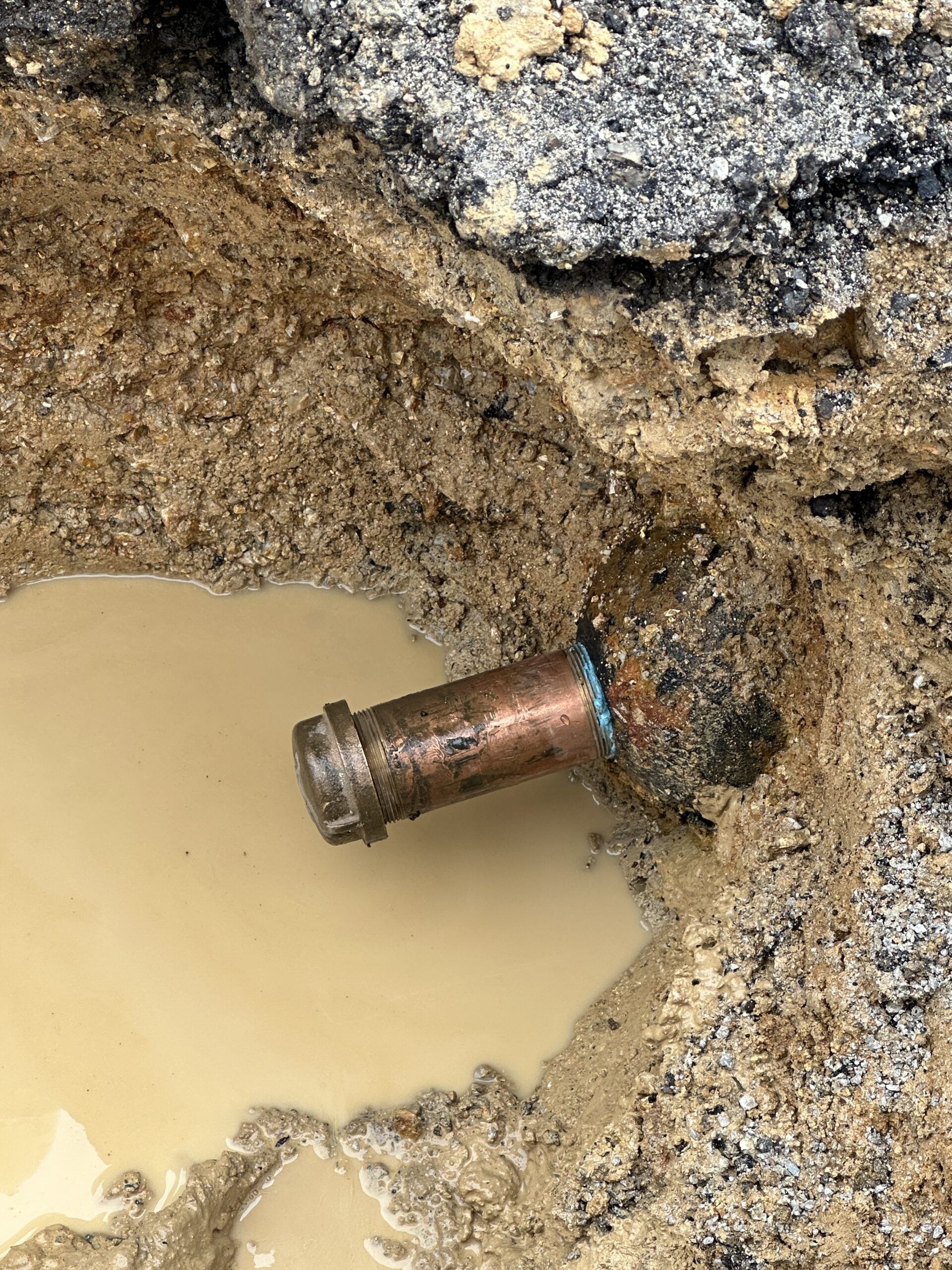 A copper pipe is sticking out of the ground in a puddle of water.