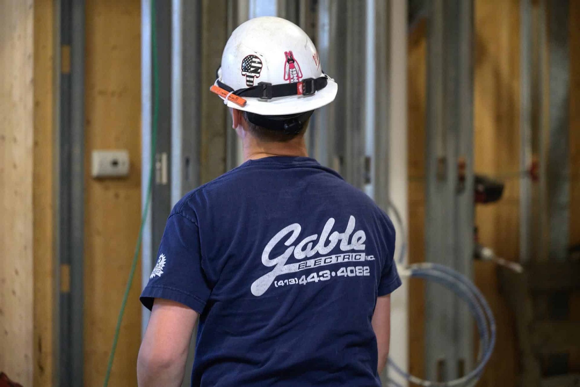 Construction worker facing away wearing a hard hat and blue shirt with "Gable" logo, inside a building.