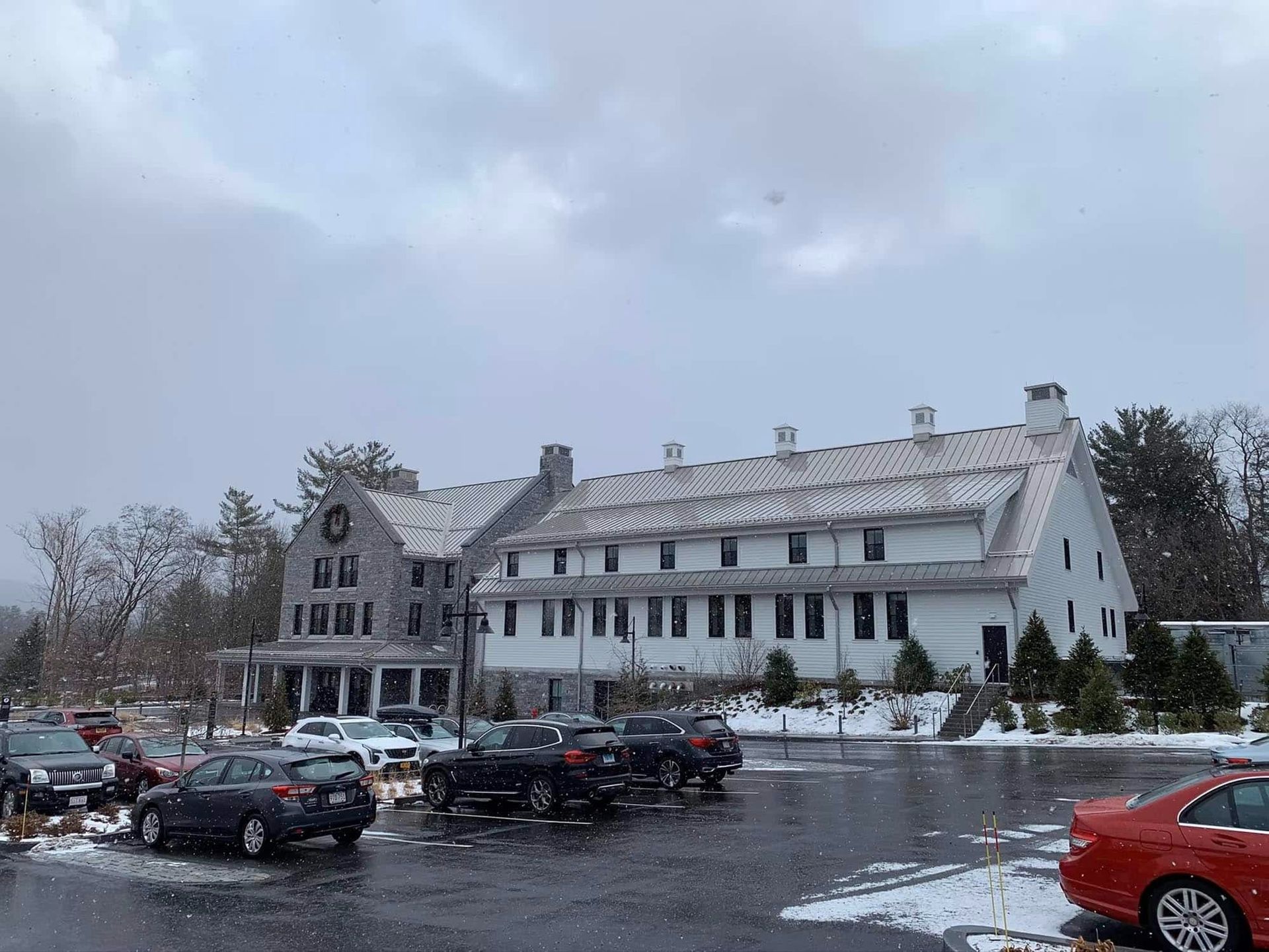 Snowy day with a two-story white building, stone facade, cars in a parking lot.