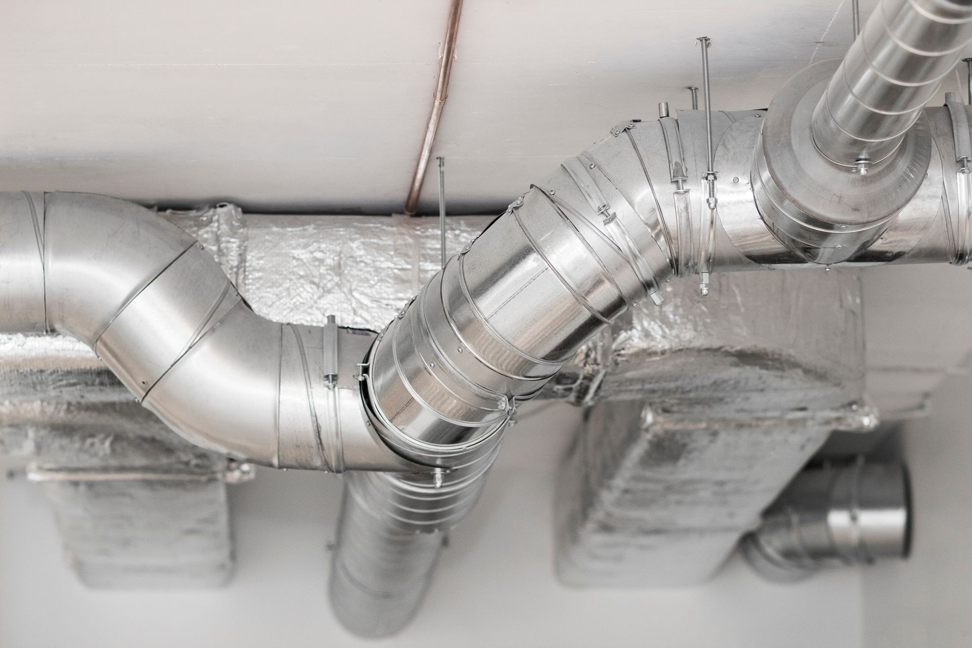 Silver HVAC ductwork branching across a white ceiling.