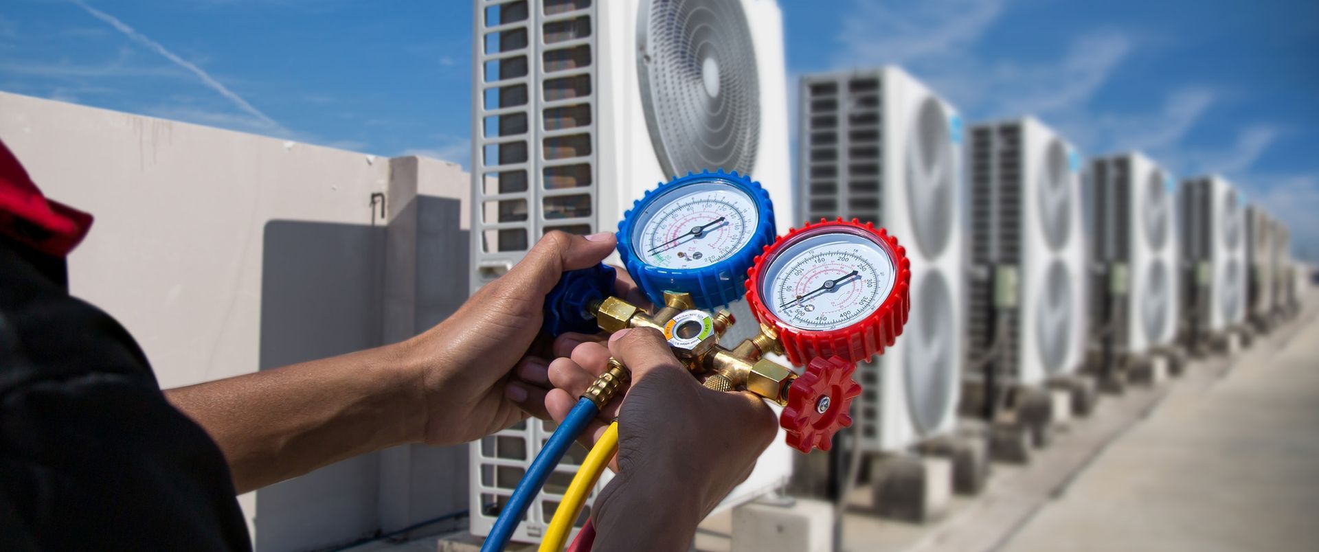 HVAC technician using gauges to service rooftop air conditioning units on a sunny day.