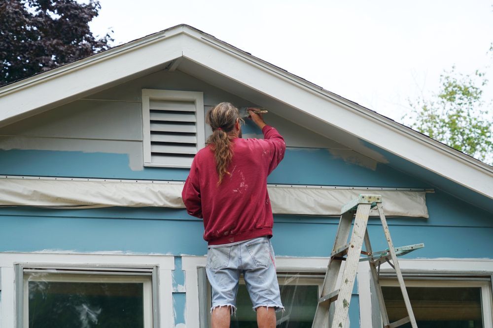 Person Painting House Trim Blue, Standing on a Ladder — Carl Whelan Building & Renovations In Woy Woy, NSW