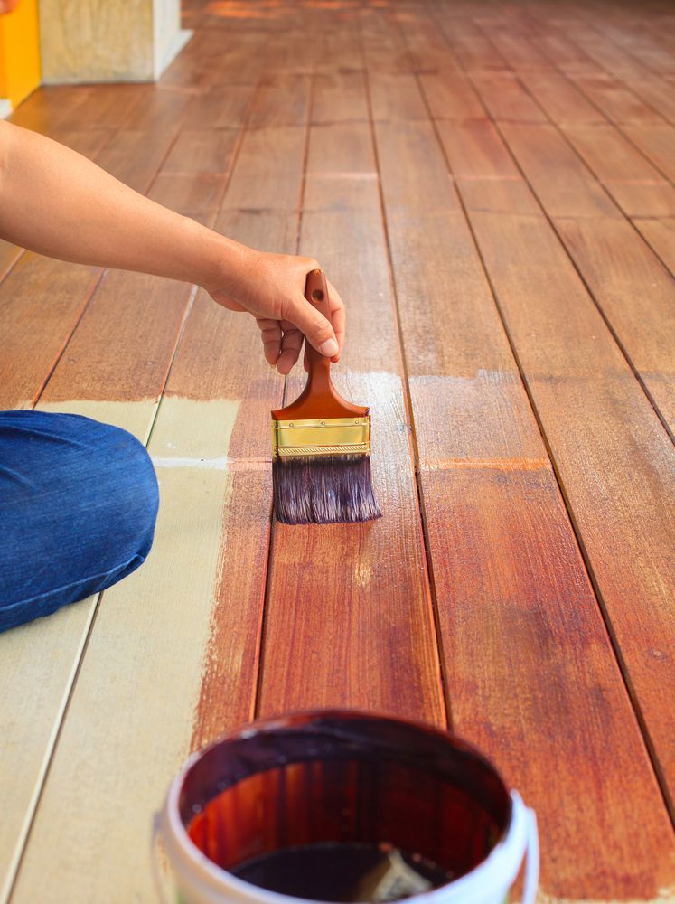 Person Applying Stain to Wooden Floorboards With a Paintbrush — Carl Whelan Building & Renovations In Wyong, NSW