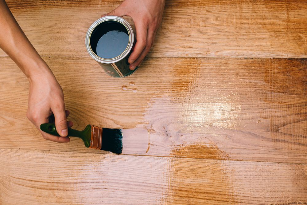 Person Applying Dark Stain to Wooden Planks With a Brush — Carl Whelan Building & Renovations In Morisset, NSW