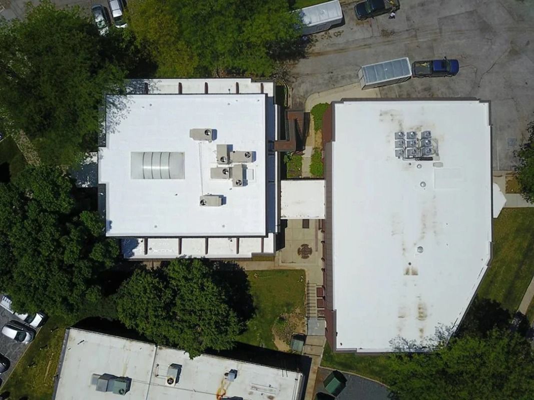 An aerial view of a building with a white roof surrounded by trees.