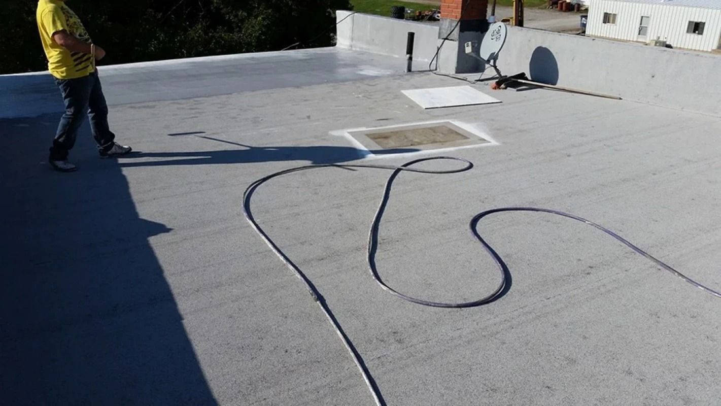 A man in a yellow shirt is standing on a roof with a hose.