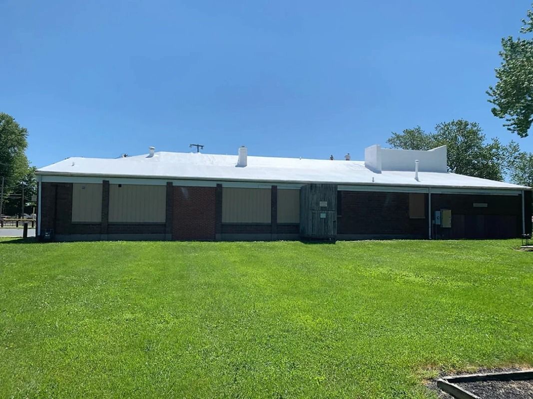 A large building with a white roof is sitting in the middle of a lush green field.