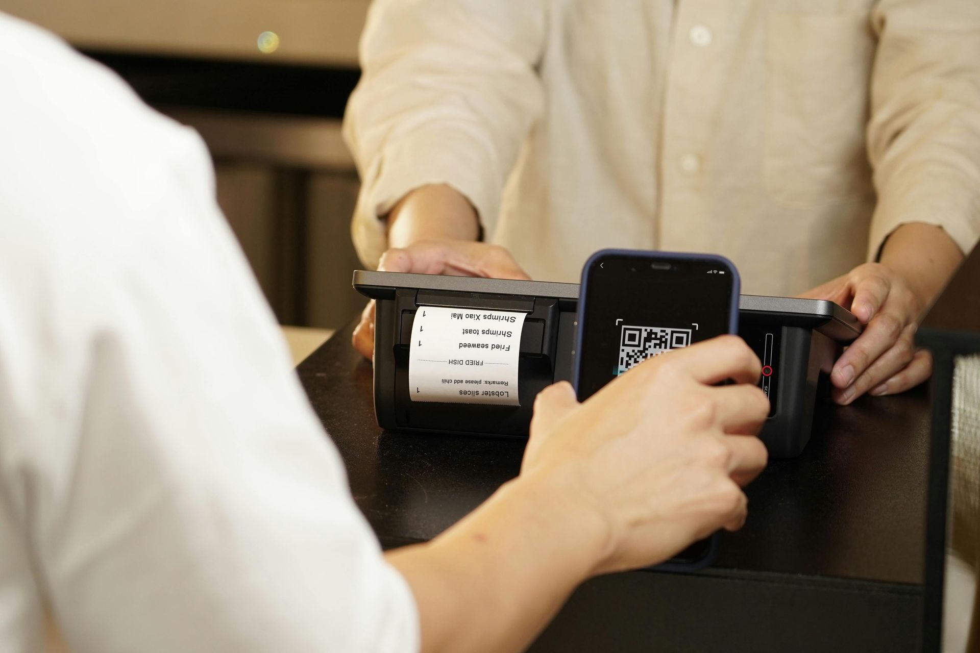 A person is holding a cell phone in front of a receipt printer.