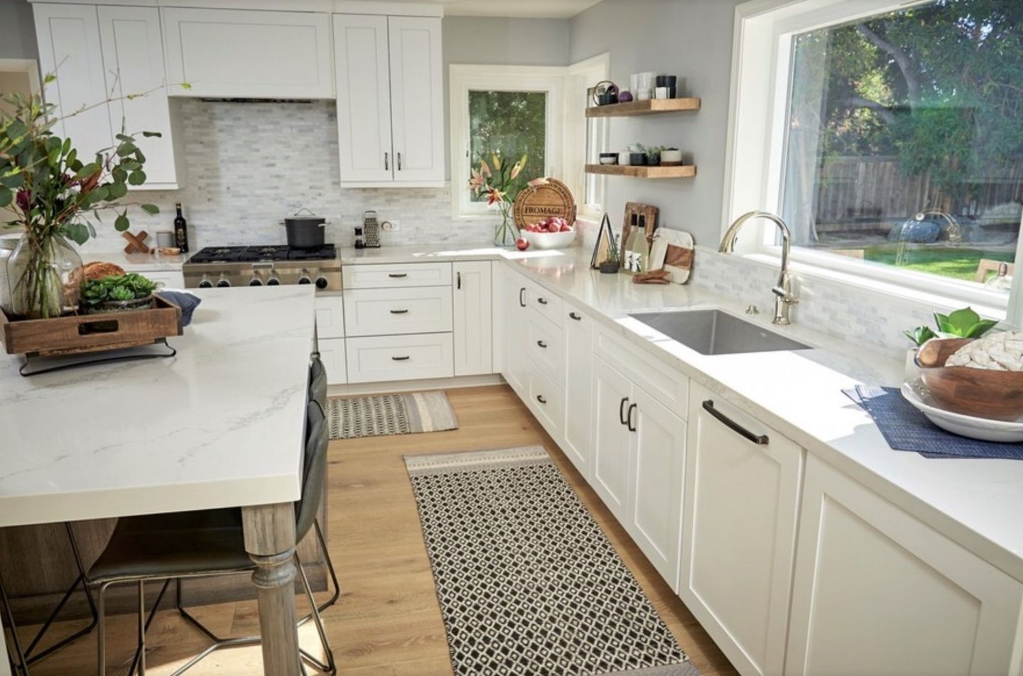 A kitchen with white cabinets , a sink , a stove and a window.