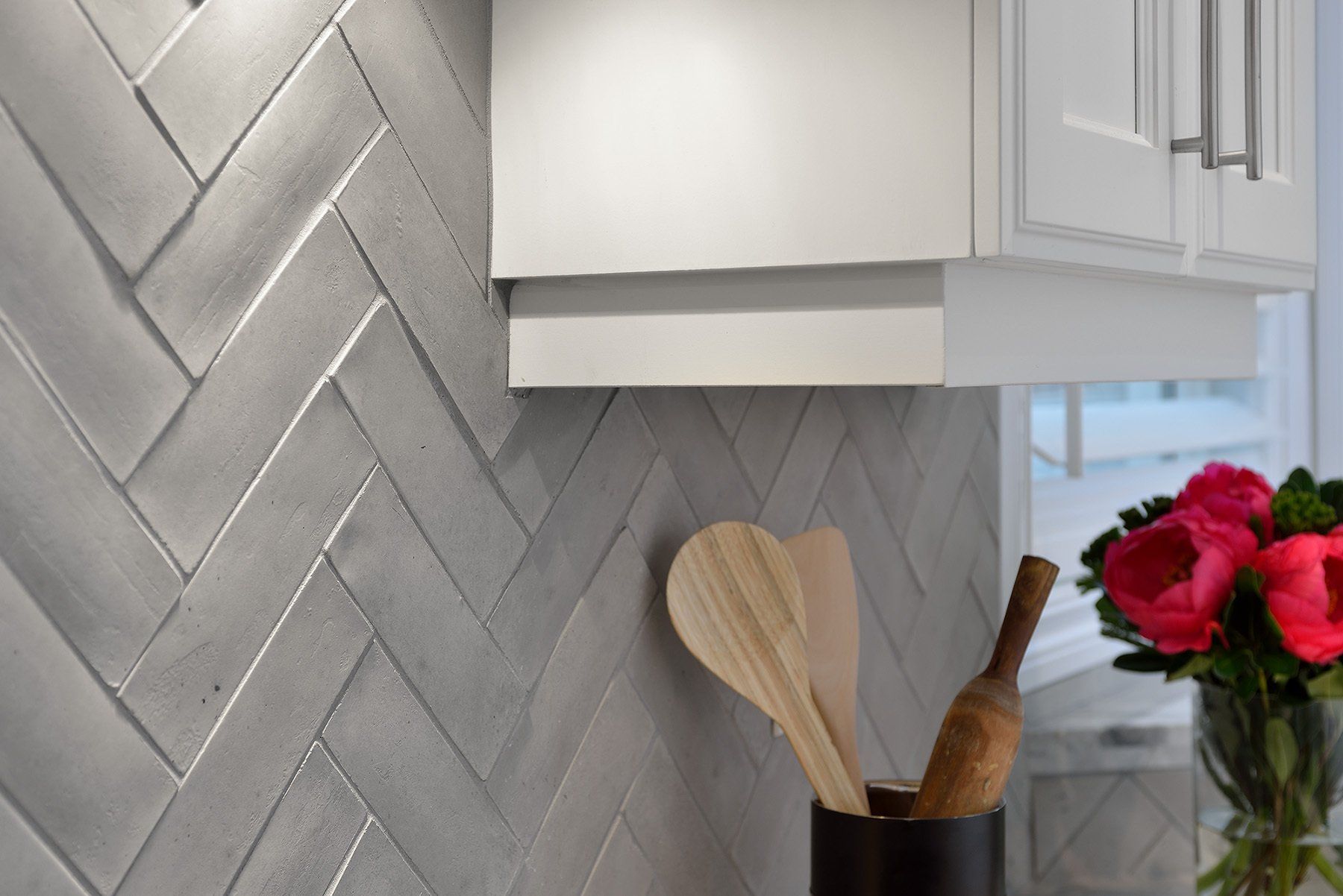 a kitchen with white cabinets and a herringbone tile wall done by remodeling contractors Remcon