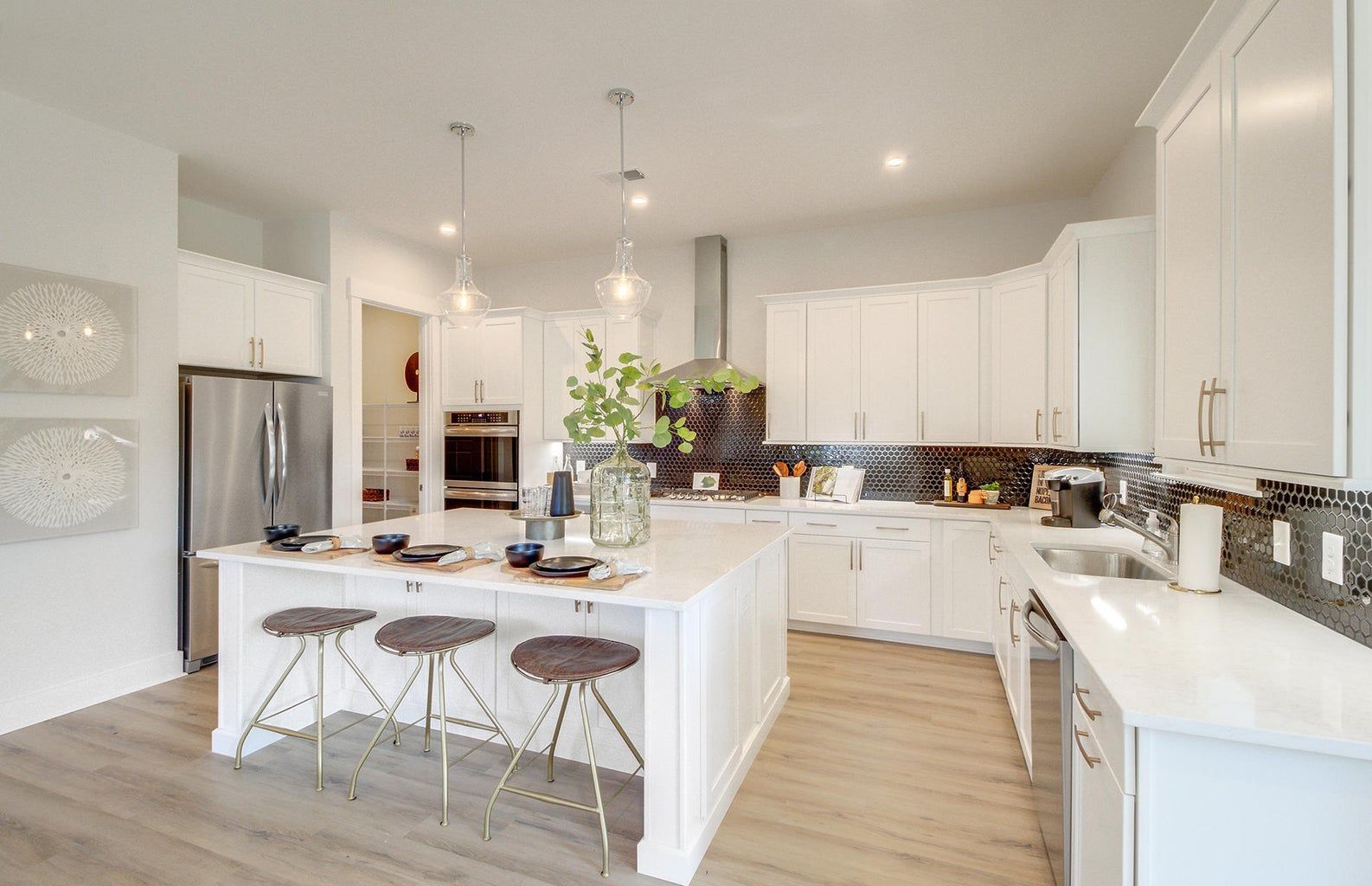 Modern white kitchen with island, stainless steel appliances, and stools.