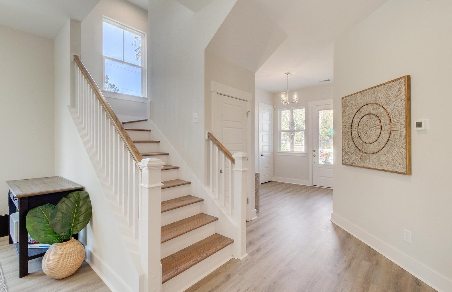 Bright entryway with staircase, wooden steps and white banister, leading to a door and art.