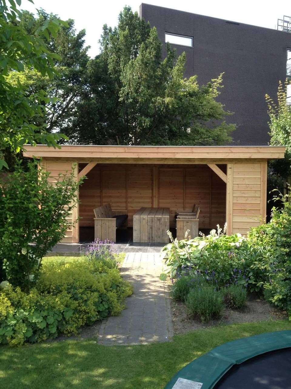 Een houten afdak met daarvoor een trampoline