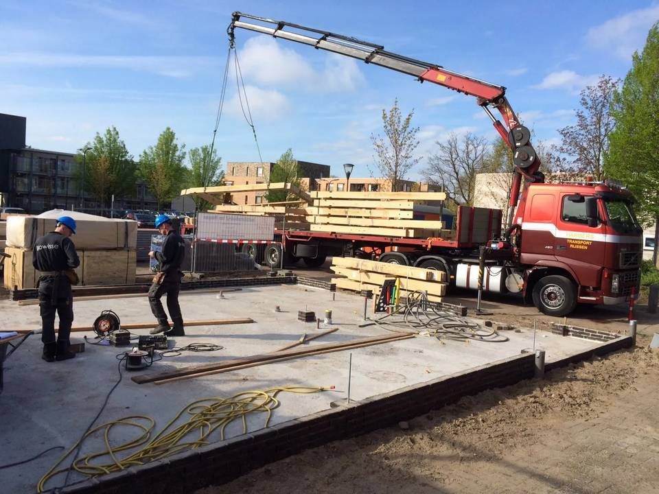 Een kraan tilt een stapel houten balken uit een vrachtwagen.