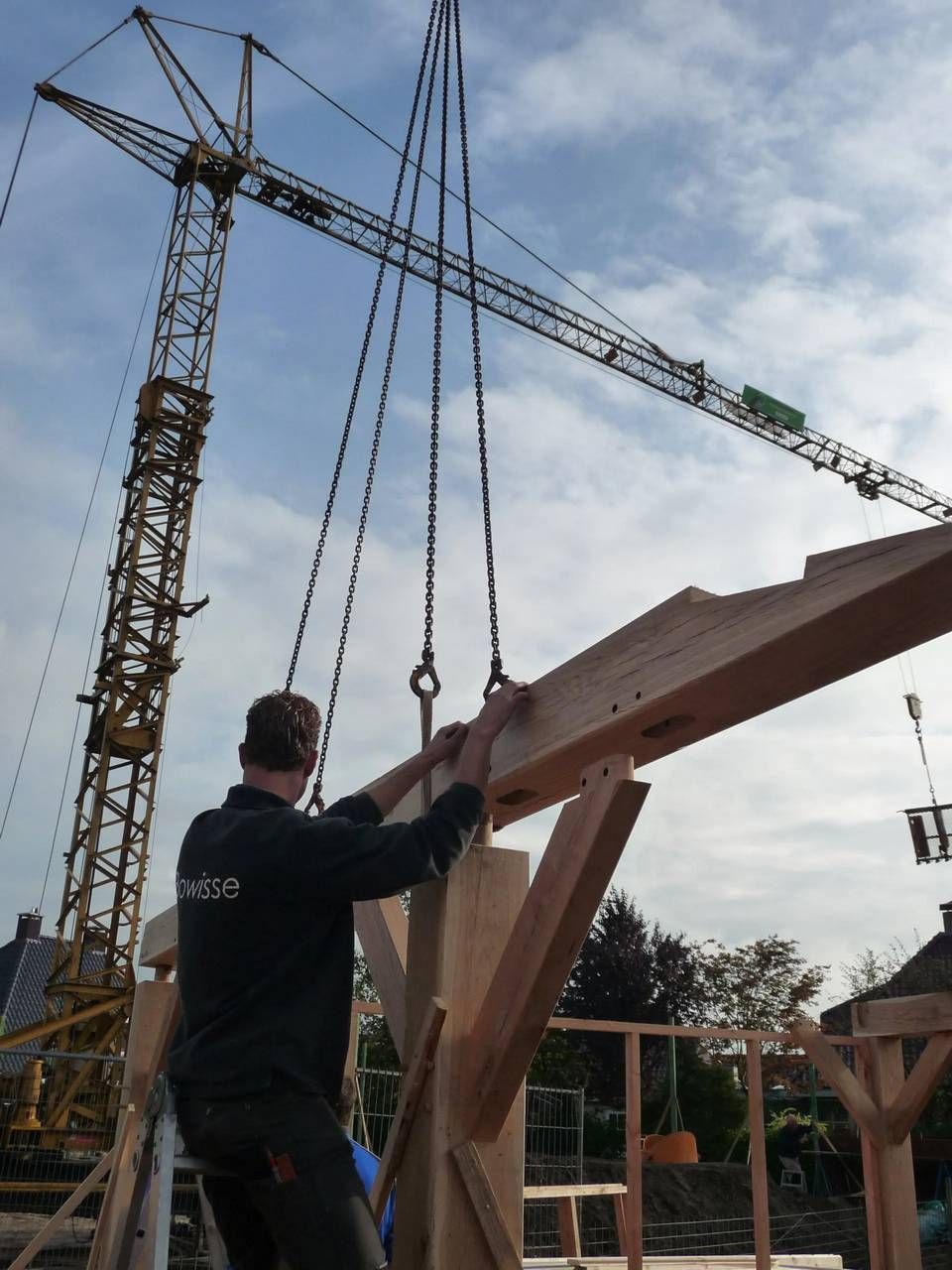 Een man werkt aan een houten constructie met een kraan op de achtergrond