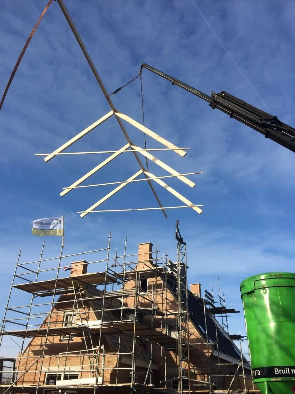 Een kraan hijst een stuk hout over een gebouw in aanbouw