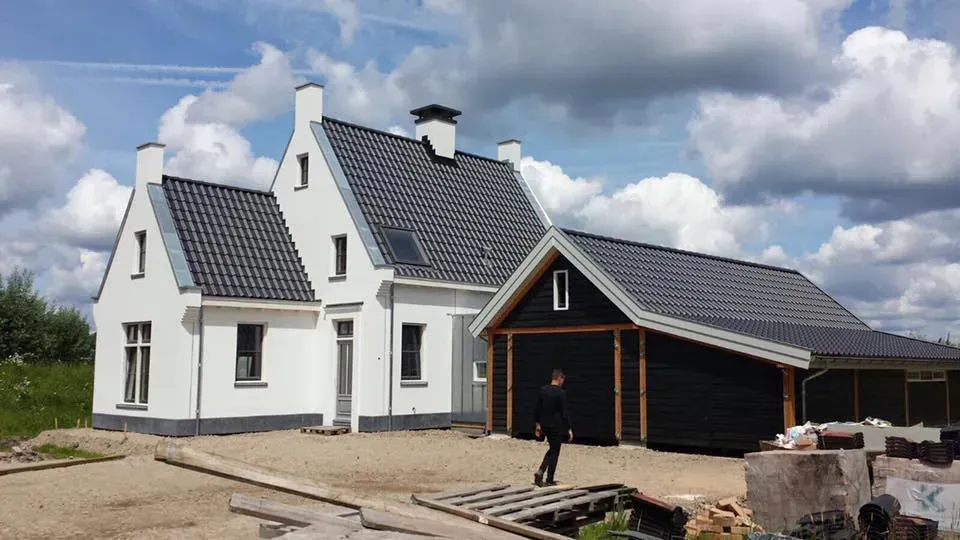 Een man loopt voor een wit huis met een zwarte garage.