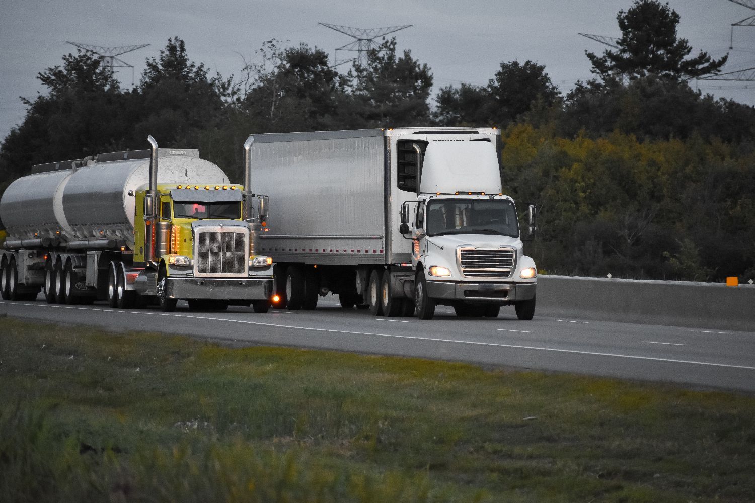 Two semi trucks are driving down a highway with trees in the background