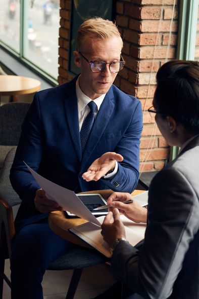 A man in a suit and tie is sitting at a table talking to another man.