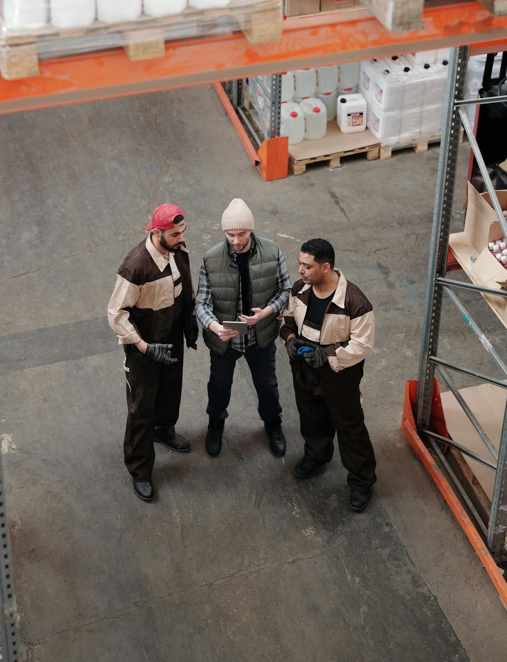 Three men are standing in a warehouse looking at a tablet.