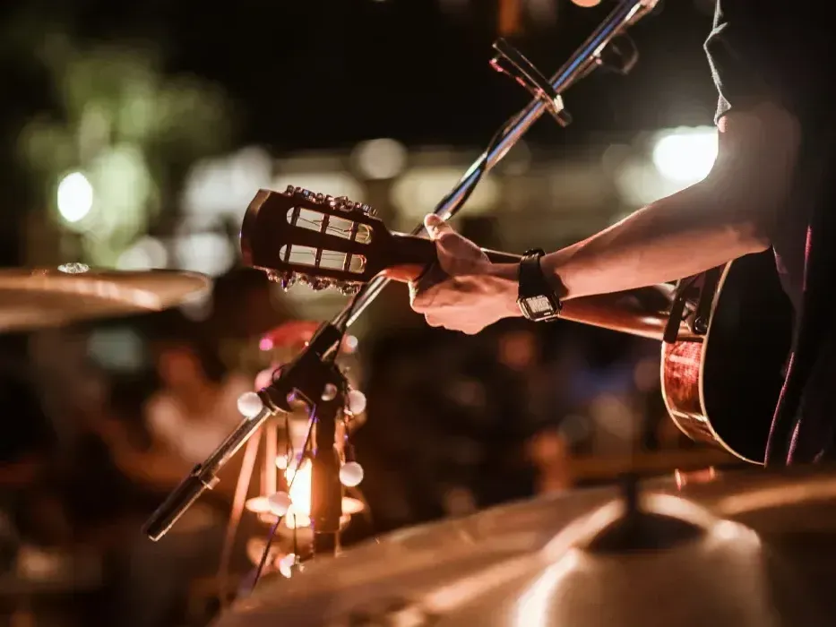 A man is playing an acoustic guitar in front of a microphone on a stage.