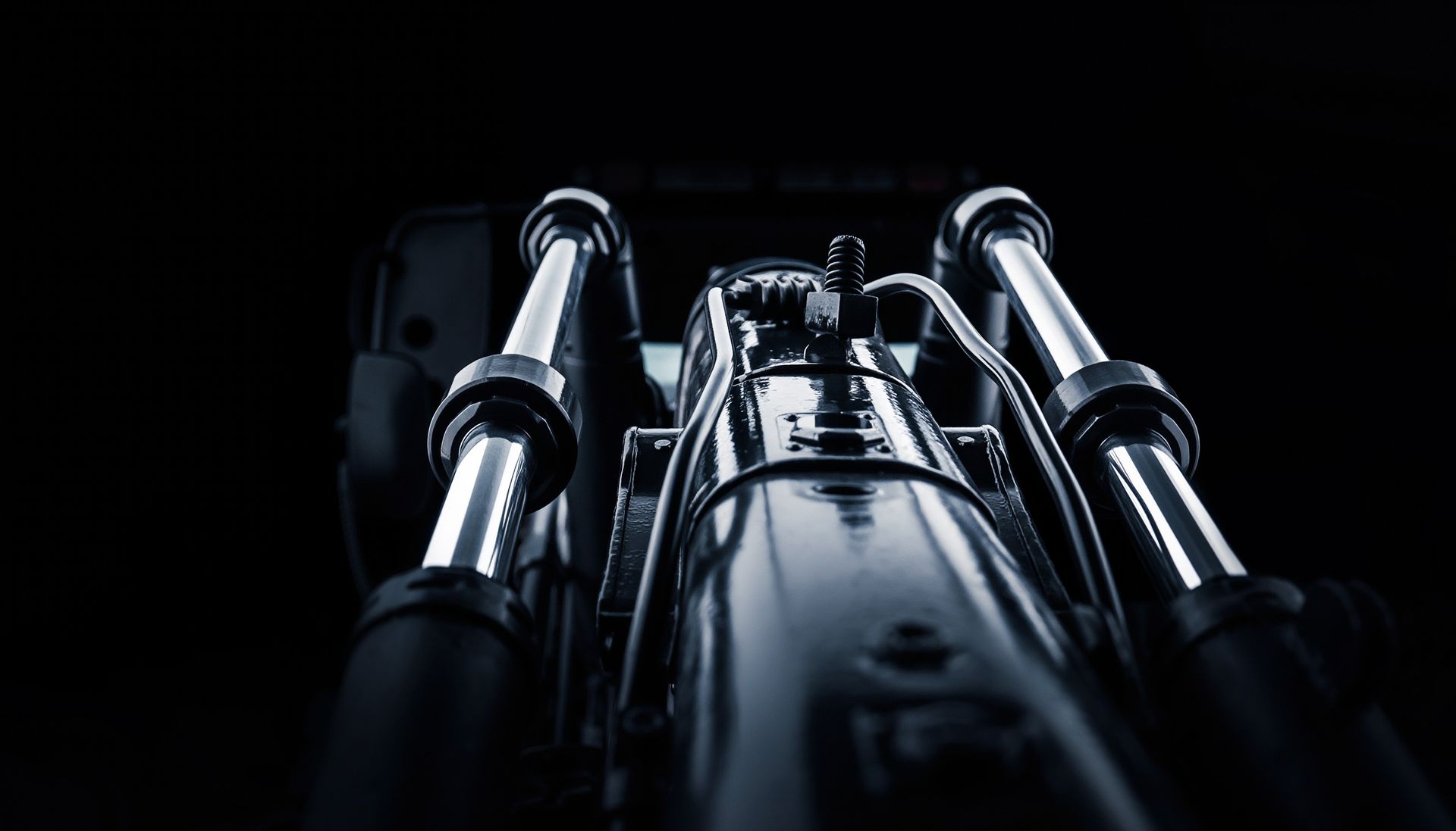 Vue rapprochée en contre-plongée d'une fourche avant métallique de moto et de son té de fourche sur fond sombre.