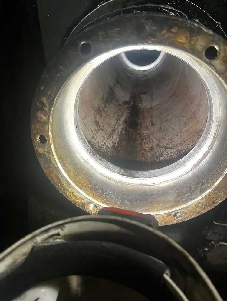 Gros plan, faiblement éclairé, de l'intérieur sombre et corrodé d'un tuyau métallique circulaire à extrémité évasée.