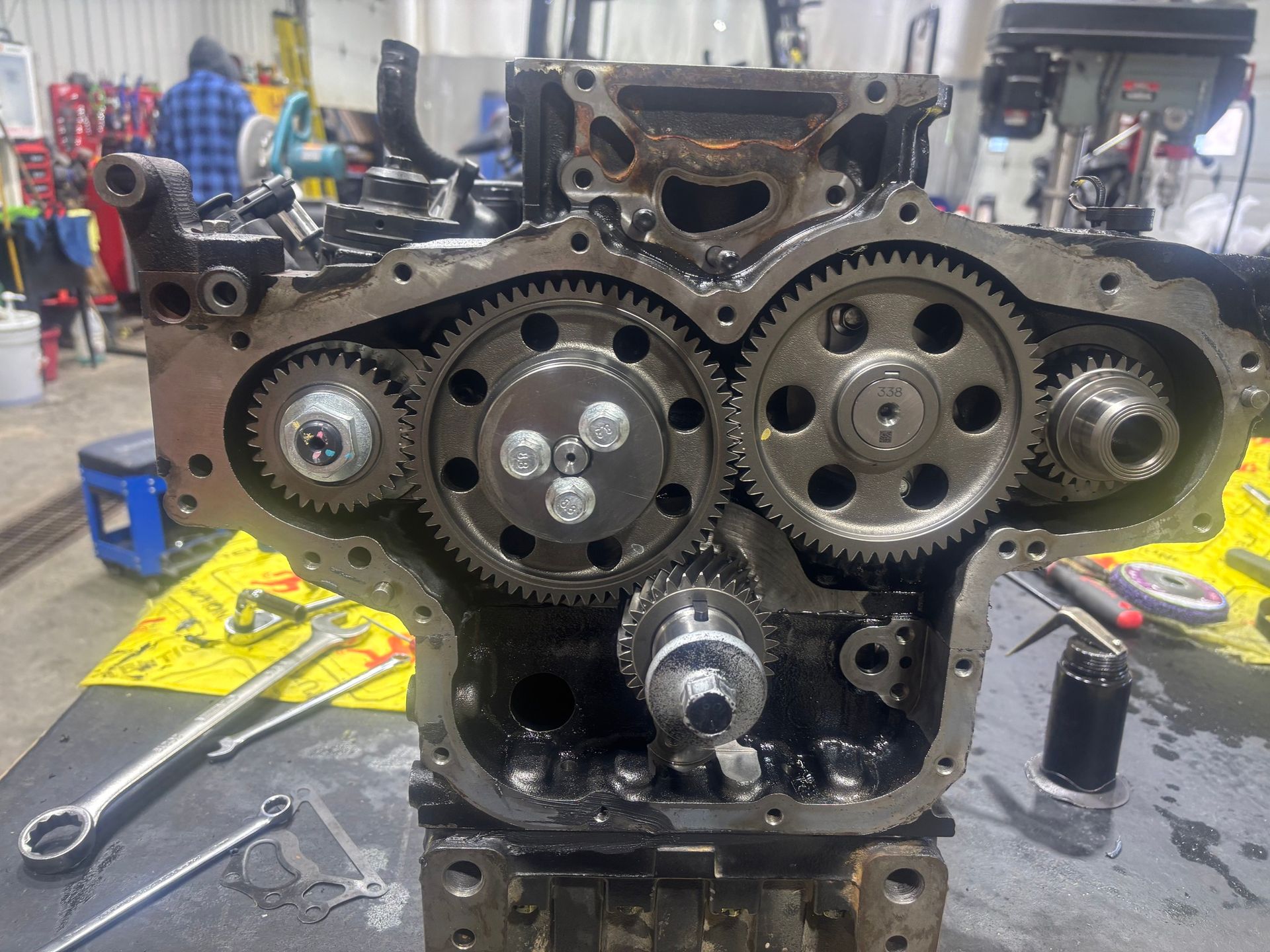 Un bloc-moteur métallique, laissant apparaître les engrenages et les composants de la distribution, repose sur une table d'atelier, entouré de divers outils.