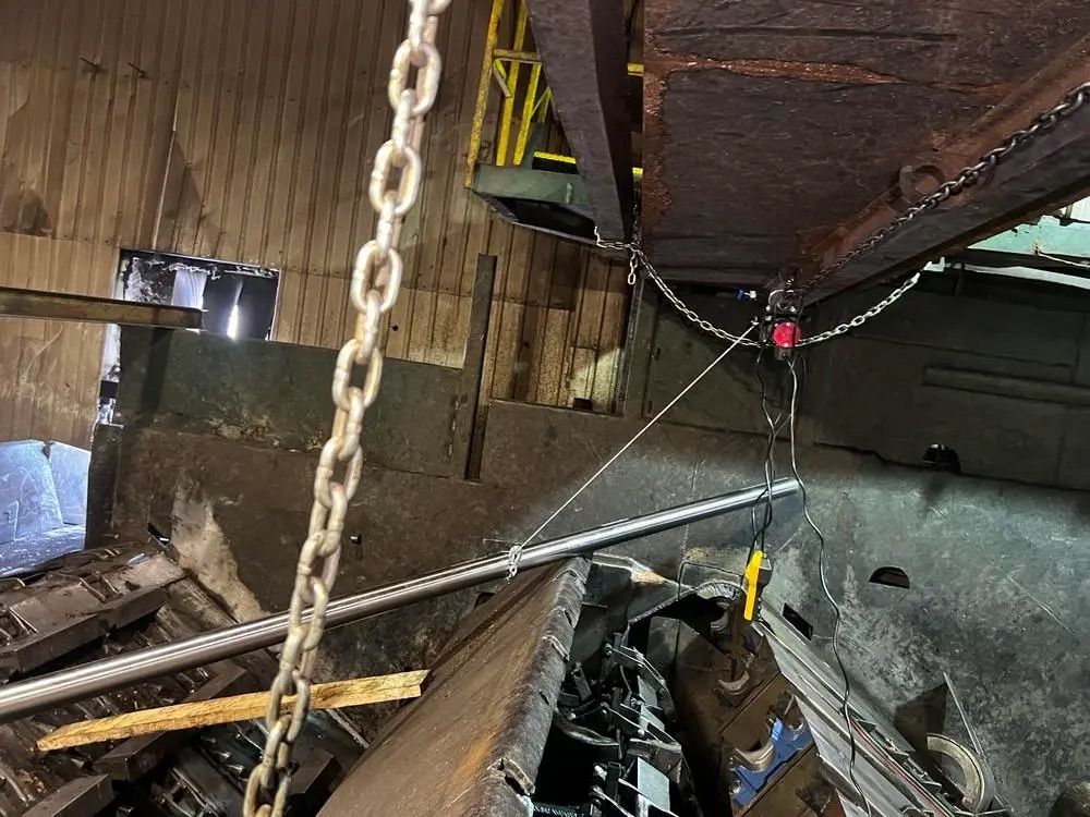 Un objet lourd en métal est suspendu par un système de chaîne et de poulie à l'intérieur d'un atelier industriel.