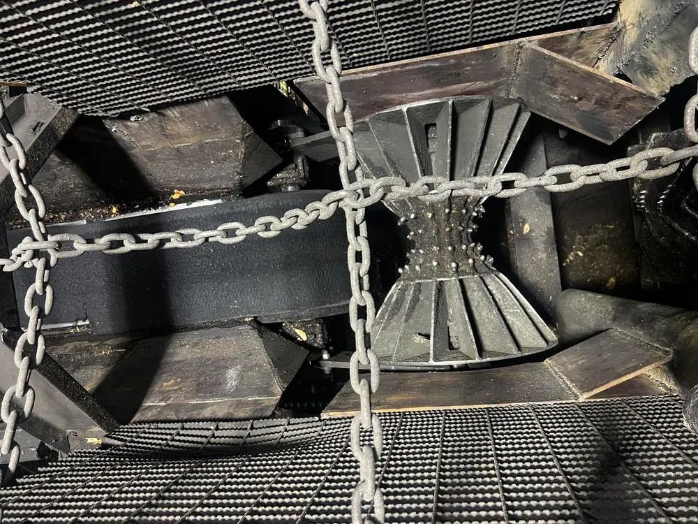 Vue aérienne d'une machine industrielle présentant un élément métallique pointu en forme de sablier, encadré par de lourdes chaînes.