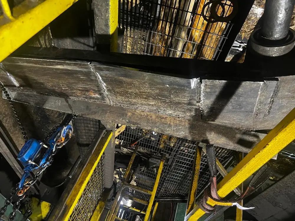 Vue en plongée sur des machines industrielles, une grille métallique, des rambardes jaunes et un palan à chaîne.