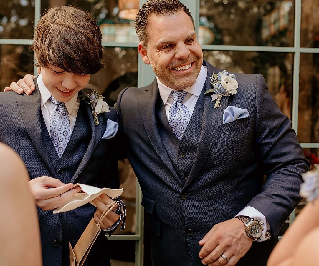 A man in a suit and tie is standing next to a boy in a suit and tie.