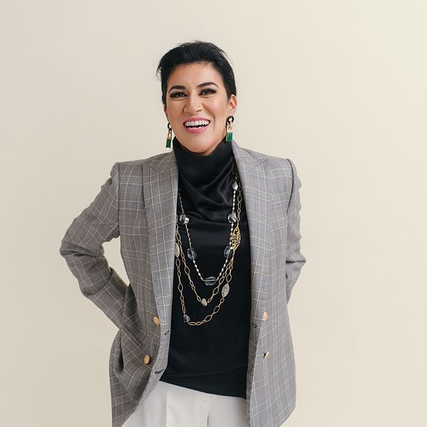 A woman wearing a plaid jacket and a black turtleneck is smiling