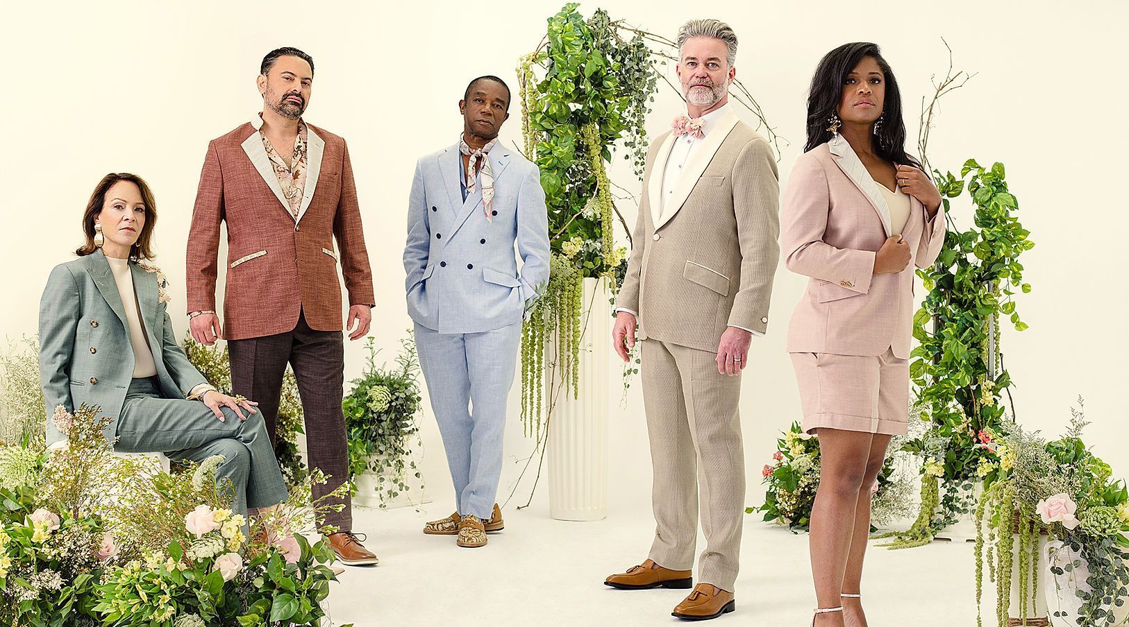A group of people in suits are standing next to each other in front of flowers.