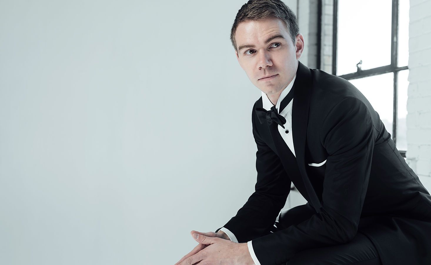 A man in a tuxedo is kneeling down in front of a window.
