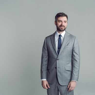 A man in a suit and tie is standing in front of a gray background.