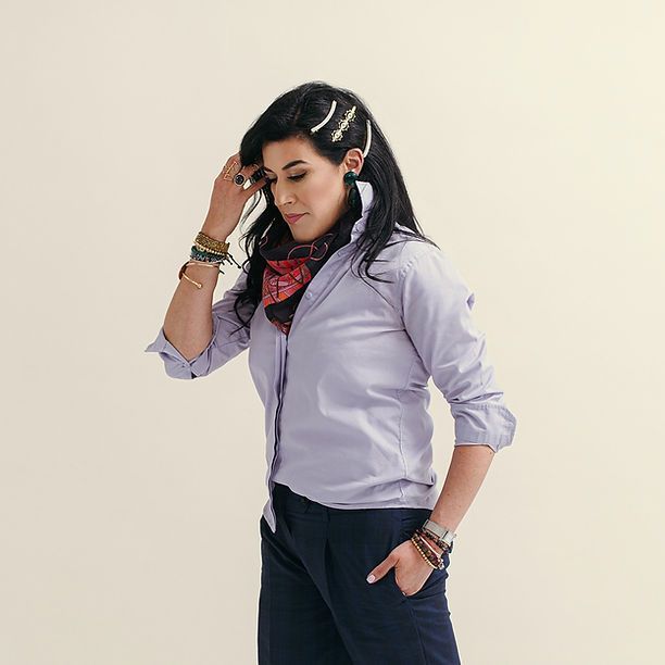 A woman wearing a purple shirt and black pants is standing with her hands in her pockets.